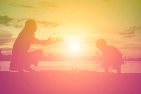 Silhouettes of mother and little daughter walking at sunsetの写真素材