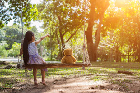 A little girl and teddy bear sitting on a swing.の写真素材