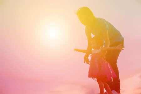a silhouette of a happy young girl child the arms of his loving mother for a hug, in front of the sunset in the sky on a summer day.の写真素材
