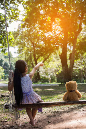 A little girl and teddy bear sitting on a swing.の写真素材