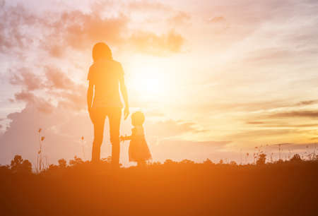 a silhouette of a happy young girl child the arms of his loving mother for a hug, in front of the sunset in the sky on a summer day.の写真素材