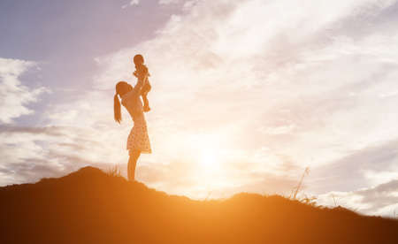 Silhouettes of mother and little daughter walking at sunsetの写真素材
