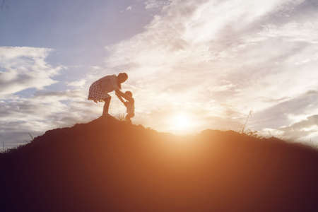 Silhouettes of mother and little daughter walking at sunsetの写真素材