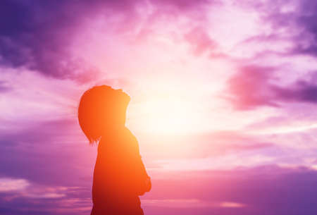Silhouette of woman praying over beautiful sky backgroundの写真素材