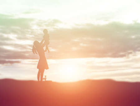 a silhouette of a happy young girl child the arms of his loving mother for a hug, in front of the sunset in the sky on a summer day.の写真素材