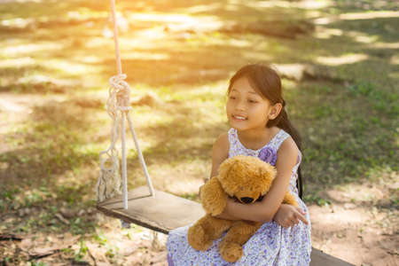 Cute little girl sitting swings , teddy bear sitting with her,little girl pointed to the tree.の写真素材