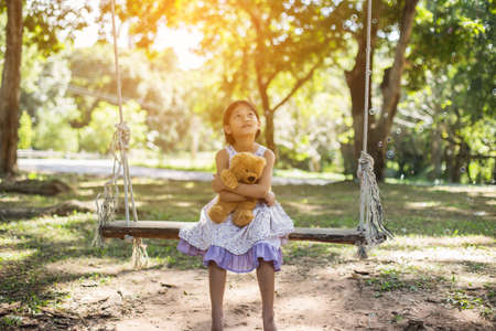 Cute little girl sitting swings , teddy bear sitting with her,little girl pointed to the tree.の写真素材