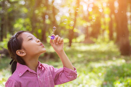 Cute little girl wearing a pink shirt blowing bubbles in the park,vintage style.