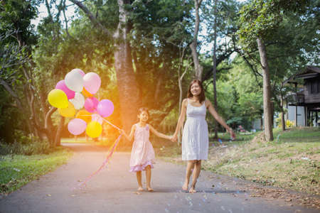 Cute little girl holding colorful balloons, running in the meadow against blue sky and clouds.の写真素材