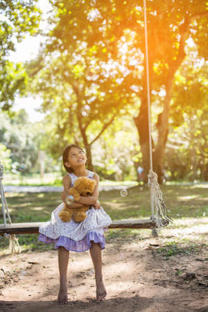 Cute little girl sitting swings , teddy bear sitting with her,little girl pointed to the tree.の写真素材