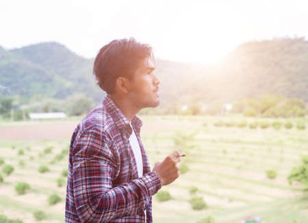 Hipster man smoking cigarette, standing behind a mountain. Among the fresh air in the morning.の写真素材