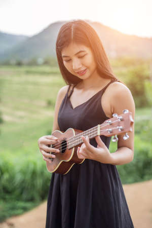 Beautiful woman holding a guitar on his shoulder, Nature park summer outside.の写真素材