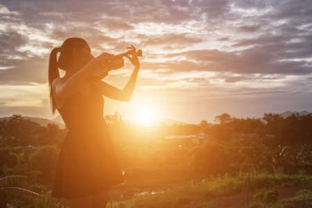 Young woman playing the violin With mountains in the backgroundの写真素材