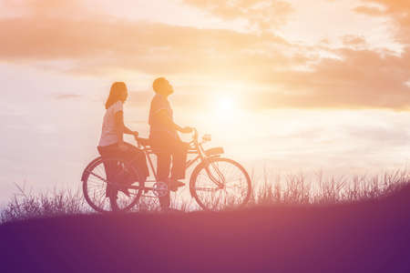 silhouette of sweet young couple in love happy time on bicycleの写真素材