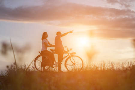 silhouette of sweet young couple in love happy time on bicycleの写真素材