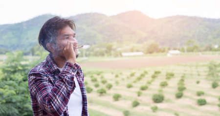Hipster man smoking cigarette, standing behind a mountain. Among the fresh air in the morning.の写真素材