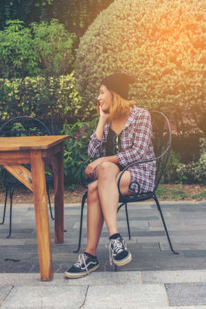 Outdoor portrait of young hipster woman sitting alone at old city cafe and waiting for her boyfriend wearing plaid outfit and sunglasses.の写真素材