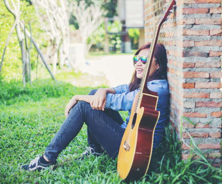 Hipster man playing guitar for his girlfriend outdoor against brick wall, enjoying together.の写真素材