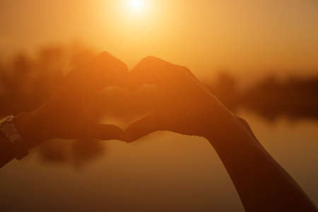 hands forming a heart shape with sunset silhouetteの写真素材