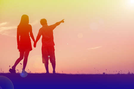 silhouette of a man and woman holding hands with each other, walking together.の写真素材