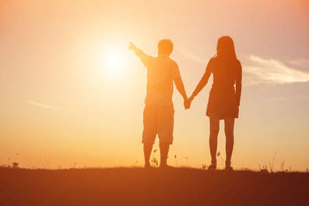 silhouette of a man and woman holding hands with each other, walking together.の写真素材