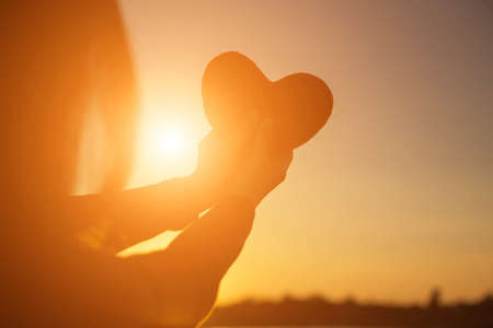 hands forming a heart shape with sunset silhouetteの写真素材