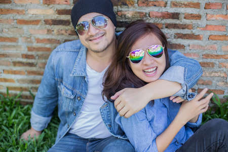 Hipster man playing guitar for his girlfriend outdoor against brick wall, enjoying together.の写真素材