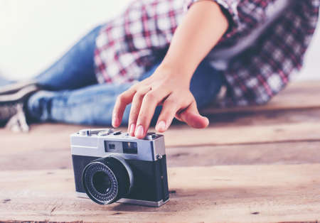 Young hipster photographer woman taking photo and look at camera sitting on wooden floor.の写真素材