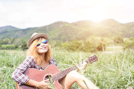Young hipster girl sitting playing a guitar and singing.の写真素材