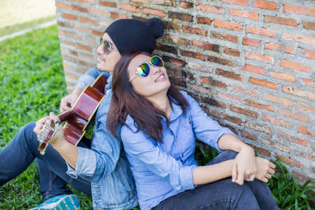 Hipster man playing guitar for his girlfriend outdoor against brick wall, enjoying together.の写真素材