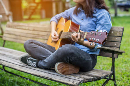 Beautiful young woman playing guitar sitting on bench, Happy time concept.の写真素材