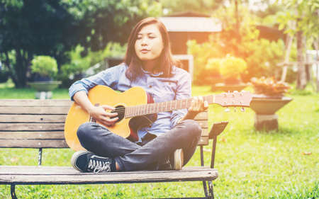 Beautiful young woman playing guitar sitting on bench, Happy time concept.の写真素材