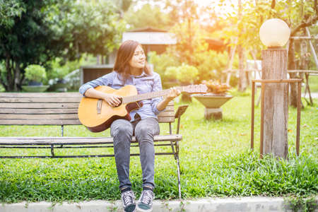 Beautiful young woman playing guitar sitting on bench, Happy time concept.の写真素材