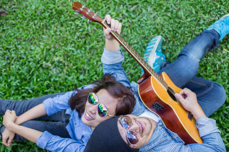 Hipster man playing guitar for his girlfriend outdoor against brick wall, enjoying together.の写真素材