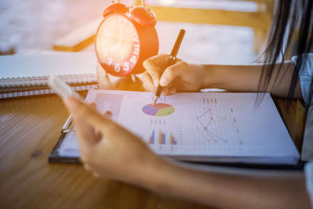 Businessman checking graph with a laptop, phone and alarm clock on the table when the morning light.の写真素材