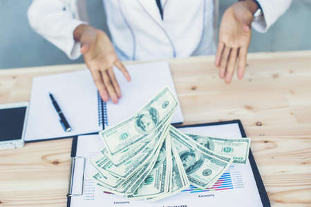 Business woman gripping The United States hundred-dollar bills in her hand and some put on the table full with business charts and notebookの写真素材