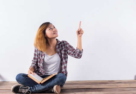 Young hipster woman holding books and pointing up on isolated white background.の写真素材