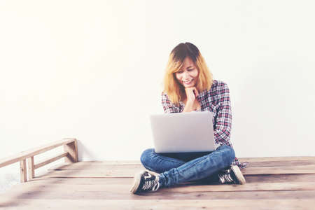 Young hipster woman sitting on wooden floor with crossed legs and using laptop on white backgroundの写真素材
