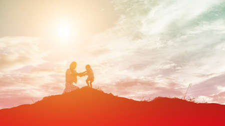 Mother encouraged her daughter out of the shadows at sunset.の写真素材