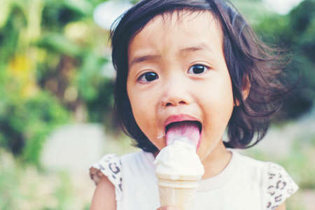 Little curly girl with ice cream on colorful backgroundの写真素材
