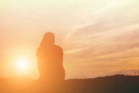Silhouette of woman praying over beautiful sky backgroundの写真素材