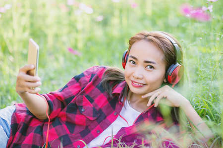A young girl lying on the grass listening to music, relax on soft and blurred backgroundの写真素材