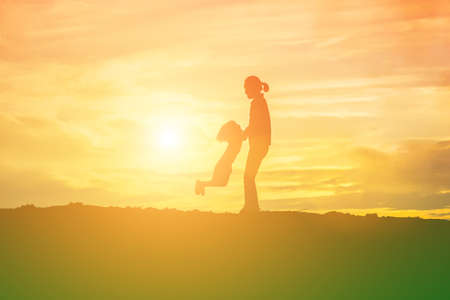 Mother encouraged her daughter out of the shadows at sunset.の写真素材