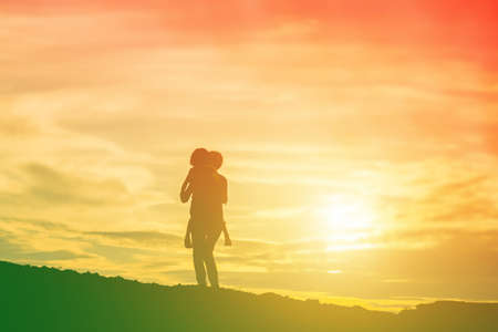 Mother encouraged her daughter out of the shadows at sunset.の写真素材