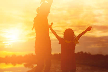 Mother encouraged her daughter out of the shadows at sunset.の写真素材