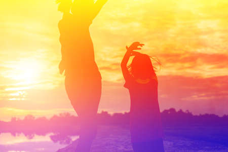 Mother encouraged her daughter out of the shadows at sunset.の写真素材
