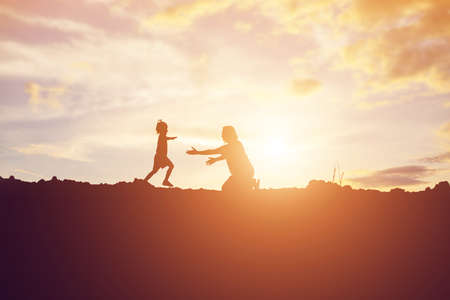 Mother encouraged her daughter out of the shadows at sunset.の写真素材