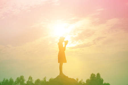 Silhouette of woman praying over beautiful sky backgroundの写真素材