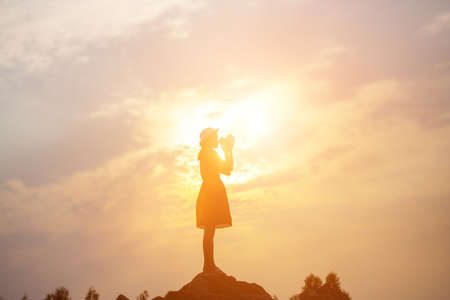 Silhouette of woman praying over beautiful sky backgroundの写真素材
