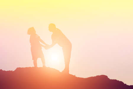 Mother encouraged her daughter out of the shadows at sunset.の写真素材